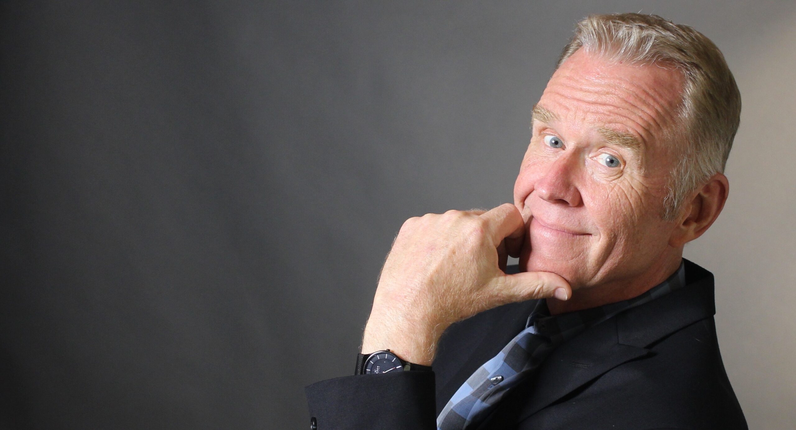 Bob Stromberg in a black suit staring at camera holding his hand to his chin