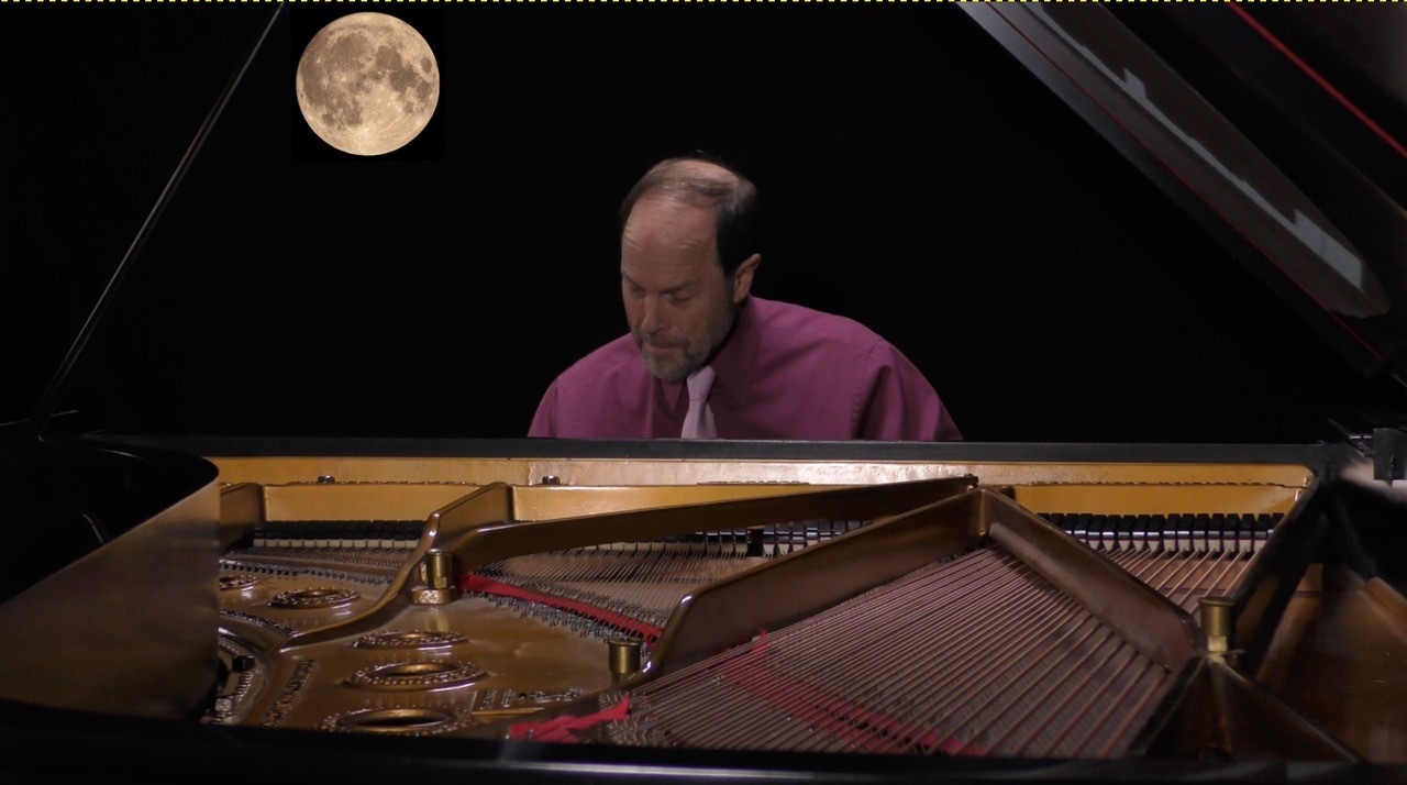 Frederick Moyer sitting and playing the piano in a purple shirt with the moon in the background